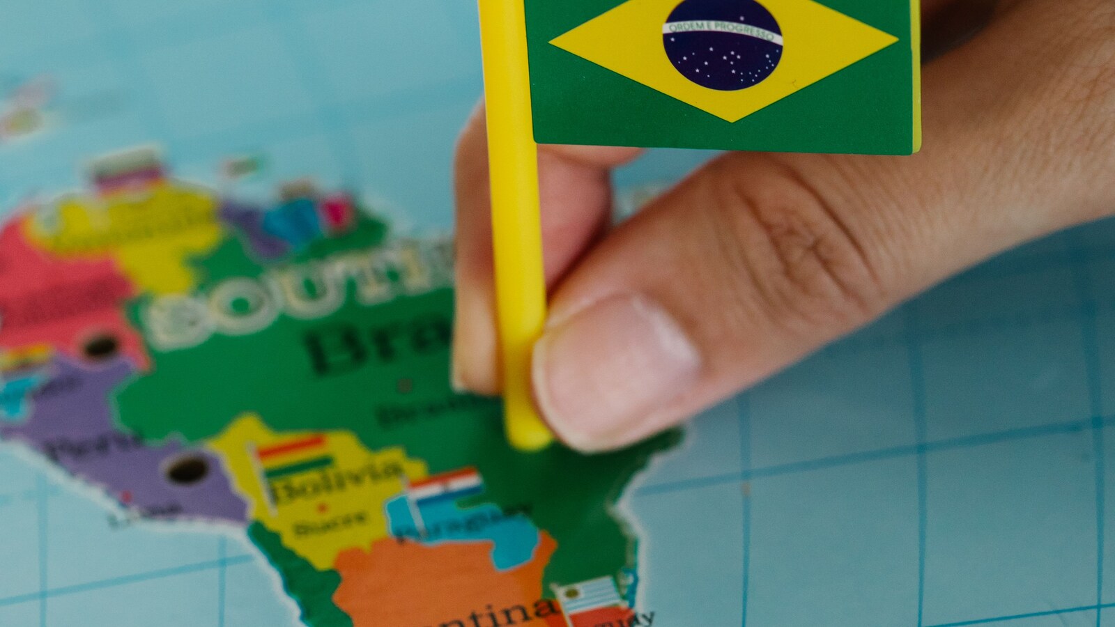 Miniatura da bandeira do Brasil posicionada sobre um mapa da América do Sul